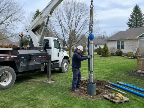 Pump hoist truck lowering a new well pump into a residential well casing